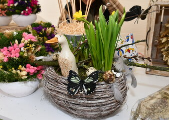 Stoisko ze stroikami świątecznymi. Koszyk w żonkilami, kaczuszka, obok kolorowe kwiatki w ceramicznym naczyniu