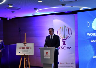 Na zdjęciu Członek Zarządu Województwa Lubelskiego Zdzisław Szwed przemawiający do mikrofonu, za jego plecami logotyp KSOW. Przed nim na sztaludze czek przedstawiający kwotę trzydzieści dwa miliony euro.