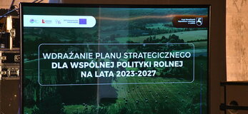 Grafika informująca o konferencji „Wdrażanie Planu Strategicznego dla Wspólnej Polityki Rolnej na lata 2023 – 2027”. Napis widnieje na tle zdjęcia pola na którym leżą bele siana i użytków zielonych, w dali widać las. Wszystko jest w tonacji ciemnozielonej.