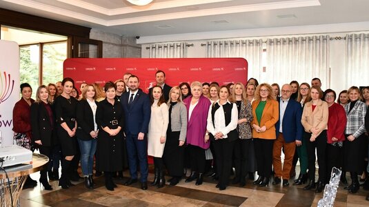 Uczestnicy konferencji stoją w sali na tle ścianki promocyjnej województwa lubelskiego