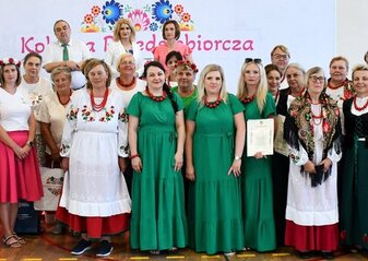 Uczestnicy półfinału konkursu Kobieta Przedsiębiorcza w powiecie opolskim stoją przed sceną. Ubrani są w regionalne stroje ludowe.