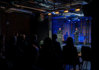 Marszałek województwa lubelskiego Jarosław Stawiarski stoi na scenie przy mównicy i mówi do uczestników konferencji „Wdrażanie Planu Strategicznego dla Wspólnej Polityki Rolnej na lata 2023 – 2027”. Obok niego stoi prowadzący konferencję.