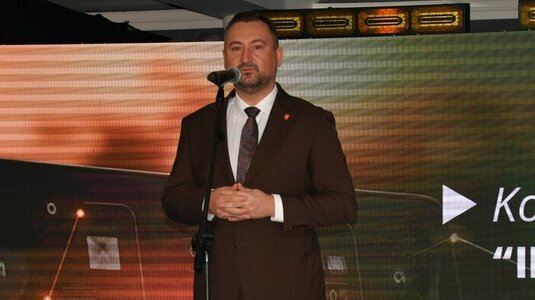 Mężczyzna ubrany elegancko stoi na scenie, przy mikrofonie na statywie. W tle wyświetla się kolorowa grafika z logotypami Unii Europejskiej, Planu Strategicznego dla Wspólnej Polityki Rolnej na lata 2023-2027, oraz napis Dofinansowane przez Unię Europejską.