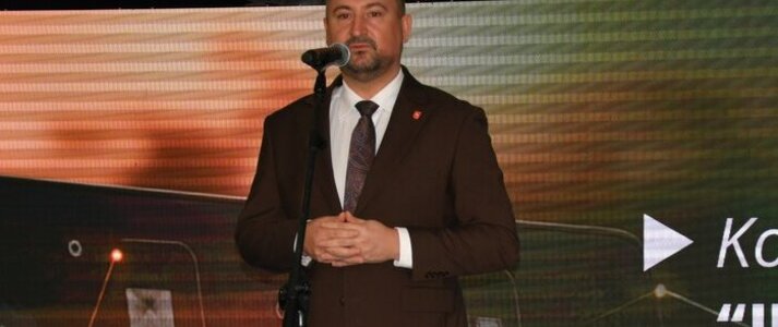 Mężczyzna ubrany elegancko stoi na scenie, przy mikrofonie na statywie. W tle wyświetla się kolorowa grafika z logotypami Unii Europejskiej, Planu Strategicznego dla Wspólnej Polityki Rolnej na lata 2023-2027, oraz napis Dofinansowane przez Unię Europejską.