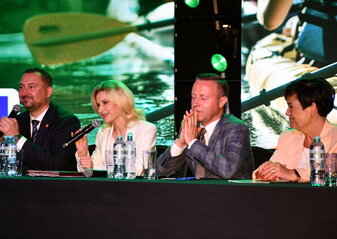 Za stołem prezydialnym podczas konferencji „Wsparcie rozwoju sportu, rekreacji i turystyki na obszarach wiejskich województwa lubelskiego w ramach Planu Strategicznego dla Wspólnej Polityki Rolnej na lata 2023–2027 – LEADER”, siedzą cztery osoby: od lewej strony wicemarszałek województwa lubelskiego Marek Wojciechowski, dyrektor Departamentu Rolnictwa i Rozwoju Obszarów Wiejskich Urzędu Marszałkowskiego Województwa Lubelskiego w Lublinie - Ewa Szałachwiej, radny województwa lubelskiego Michał Mulawa i zastępca dyrektora Departamentu Rolnictwa i Rozwoju Obszarów Wiejskich Urzędu Marszałkowskiego Województwa Lubelskiego w Lublinie – Dorota Kozak. Do uczestników konferencji przez mikrofon mówi dyrektor Ewa Szałachwiej.
