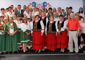 Wszyscy uczestnicy półfinału konkursu Kobieta przedsiębiorcza stoją przed sceną. Panie z kół gospodyń wiejskich ubrane sa w regionalne stroje ludowe