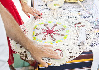 Zdjęcie przedstawia leżącą na stole serwetę okrągłą z haftowanym środkiem, na niej oparte ręce
