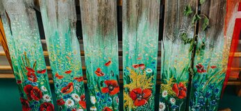 Płot z desek pomalowanych na dole w polne kwiaty: maki, chabry oraz rumiany. Im wyżej tym elementy namalowane są coraz delikatniejsze, w połowie zacierają się z naturalnym kolorem drewna.