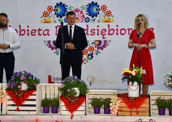 Trzy osoby stoją na scenie udekorowanej kwiatami. Jest to od lewej: Jacek Pożarowszczyk, Wicestarosta Powiatu Lubartowskiego, Zdzisław Szwed, Członek Zarządu Województwa Lubelskiego i Ewa Szałachwiej, Dyrektor Departamentu Rolnictwa i Rozwoju Obszarów Wiejskich. W tle widać białą ściankę z sercem z kwiatów w motywie folkowym i napisem przez środek serca :Kobieta Przedsiębiorcza"