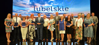 Partnerzy Krajowej Sieci Obszarów Wiejskich, którzy podpisali umowy w ramach Konkursu dla Partnerów KSOW nr 6/2022. Wśród nich Członek Zarządu Województwa Lubelskiego Zdzisław Szwed oraz Dyrektor Departamentu Rolnictwa i Rozwoju Obszarów Wiejskich Ewa Szałachwiej. W tle ścianka przedstawiająca zachód słońca nad polem z dojrzałym zbożem, na górze napis lubelskie. Partnerzy trzymają w ręku niebieskie teczki z umowami.