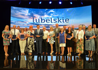 Partnerzy Krajowej Sieci Obszarów Wiejskich, którzy podpisali umowy w ramach Konkursu dla Partnerów KSOW nr 6/2022. Wśród nich Członek Zarządu Województwa Lubelskiego Zdzisław Szwed oraz Dyrektor Departamentu Rolnictwa i Rozwoju Obszarów Wiejskich Ewa Szałachwiej. W tle ścianka przedstawiająca zachód słońca nad polem z dojrzałym zbożem, na górze napis lubelskie. Partnerzy trzymają w ręku niebieskie teczki z umowami.