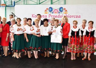 Grupa około 20 osób stoi przed sceną. Są to laureaci półfinału konkursu "Kobieta Przedsiębiorcza"