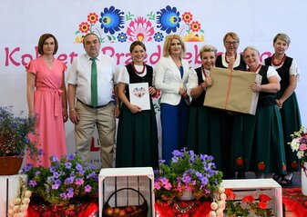 Na scenie stoją Panie z Koła które zajęło trzecie miejsce w półfinale Konkursu Kobieta Przedsiębiorcza. Trzymają duże pudełko z prezentem. Wraz z nimi jest Pani Ewa Szałachwiej, Dyrektor Departamentu Rolnictwa i Rozwoju Obszarów Wiejskich