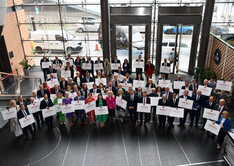 Zdjęcie grupowe przedstawiające reprezentantów gmin trzymających w rękach czeki z kwotami w polskich złotych. 