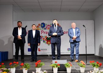 Czterech mężczyzn stoi na scenie ozdobionej kwiatami. Za nimi widać serce z kolorowych kwaitów w motywie folkowym z napisem Kobieta Przedsiębiorcza. Wśród mężczyzn jest Pan Zdzisław Szwed, Członek zarządu Województwa Lubelskiego