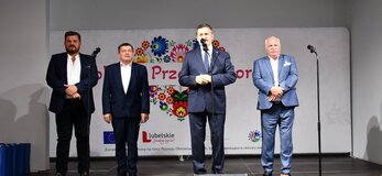 Czterech mężczyzn stoi na scenie ozdobionej kwiatami. Za nimi widać serce z kolorowych kwaitów w motywie folkowym z napisem Kobieta Przedsiębiorcza. Wśród mężczyzn jest Pan Zdzisław Szwed, Członek zarządu Województwa Lubelskiego