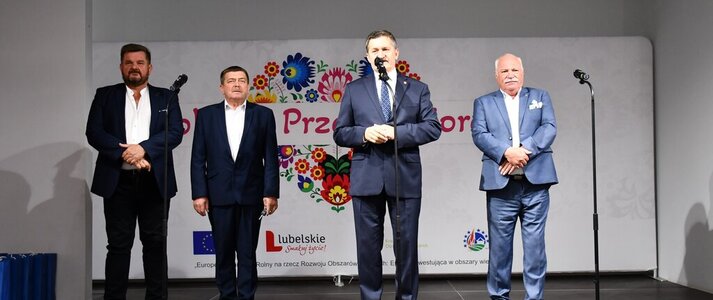 Czterech mężczyzn stoi na scenie ozdobionej kwiatami. Za nimi widać serce z kolorowych kwaitów w motywie folkowym z napisem Kobieta Przedsiębiorcza. Wśród mężczyzn jest Pan Zdzisław Szwed, Członek zarządu Województwa Lubelskiego