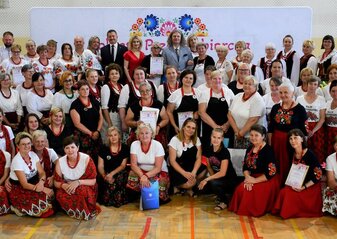 Duża grupa osób stoi na scenie. Są to uczestnicy konkursu "Kobieta Przedsiębiorcza" oraz organizatorzy. Uczestnicy ubrani są w regionalne stroje ludowe. Wśród tej grupy są Tomasz Marzęda, Starosta Powiatu Lubartowskiego, Jacek Pożarowszczyk, Wicestarosta Powiatu Lubartowskiego, Zdzisław Szwed, Członek Zarządu Województwa Lubelskiego i Ewa Szałachwiej, Dyrektor Departamentu Rolnictwa i Rozwoju Obszarów Wiejskich. W tle widać białą ściankę z sercem z kwiatów w motywie folkowym i napisem przez środek serca :Kobieta Przedsiębiorcza" 