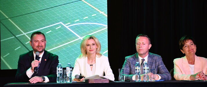 Za stołem prezydialnym podczas konferencji „Wsparcie rozwoju sportu, rekreacji i turystyki na obszarach wiejskich województwa lubelskiego w ramach Planu Strategicznego dla Wspólnej Polityki Rolnej na lata 2023–2027 – LEADER”, siedzą cztery osoby: od lewej strony wicemarszałek województwa lubelskiego Marek Wojciechowski, dyrektor Departamentu Rolnictwa i Rozwoju Obszarów Wiejskich Urzędu Marszałkowskiego Województwa Lubelskiego w Lublinie - Ewa Szałachwiej, radny województwa lubelskiego Michał Mulawa i zastępca dyrektora Departamentu Rolnictwa i Rozwoju Obszarów Wiejskich Urzędu Marszałkowskiego Województwa Lubelskiego w Lublinie – Dorota Kozak. Do uczestników konferencji przez mikrofon mówi wicemarszałek Marek Wojciechowski.