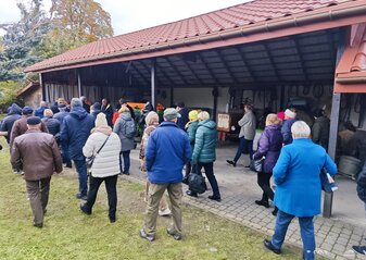 Uczestnicy wyjazdu studyjnego pod nazwą „Gospodarstwa ekologiczne” na Podlasie zwiedzają gospodarstwo. Właściciel mówi o maszynach rolniczych jakie są używane w gospodarstwie. Grupa stoi przy wiacie z narzędziami i maszynami rolniczymi.