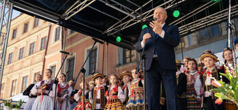 Na scenie na tle zespołu "Leszczyniacy" stoi marszałek Jarosław Stawiarki, który wita odwiedzających Jarmark Wielkanocny