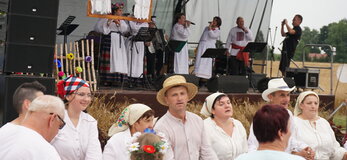 Zdjęcie przedstawia scenę z występującym zespołem folklorystycznym poniżej tańczących uczestników wydarzenia