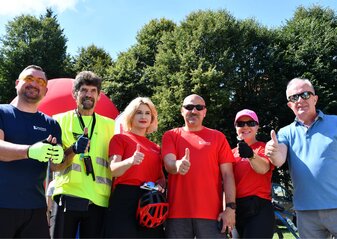 Grupa sześciu osób stoi z wyciągniętą do przodu ręką i podniesionym w górę kciukiem. Są to uczestnicy i organizatorzy rajdu po zakończonym rajdzie